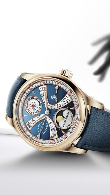 The image features the Hommage la Placide timepiece with a gold-toned case and a vibrant blue dial, resting on a clean, white surface. The watch has a blue leather strap and intricate complications visible on its face, including a moon phase indicator and other sub-dials. In the background, a blurred, dark silhouette of a hand is reaching towards the watch, creating a sense of intrigue or desire. The overall aesthetic is minimalist and elegant, highlighting the watch as the central object of focus.