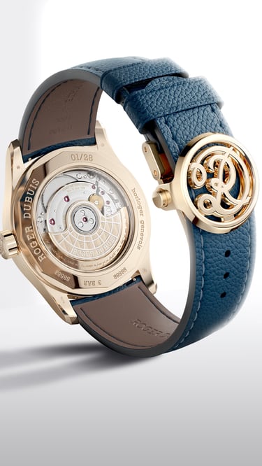 The image displays the reverse side the Hommage la Placide timepiece, featuring a rose gold-toned case and a blue leather strap. The transparent case back reveals the intricate mechanical movement of the watch. The blue strap is secured by a distinctive rose gold-toned buckle or clasp, which is intricately designed, possibly featuring a stylized logo or emblem. The watch is presented against a clean, minimalist white background, emphasizing its craftsmanship and elegant details