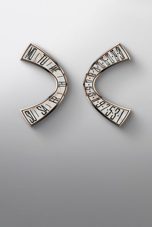 This image displays two curved, gold-toned watch components, likely calendar indicators. The left piece shows abbreviations for days of the week (MO-SU), while the right piece displays dates (1-31), both set against an iridescent inlay.