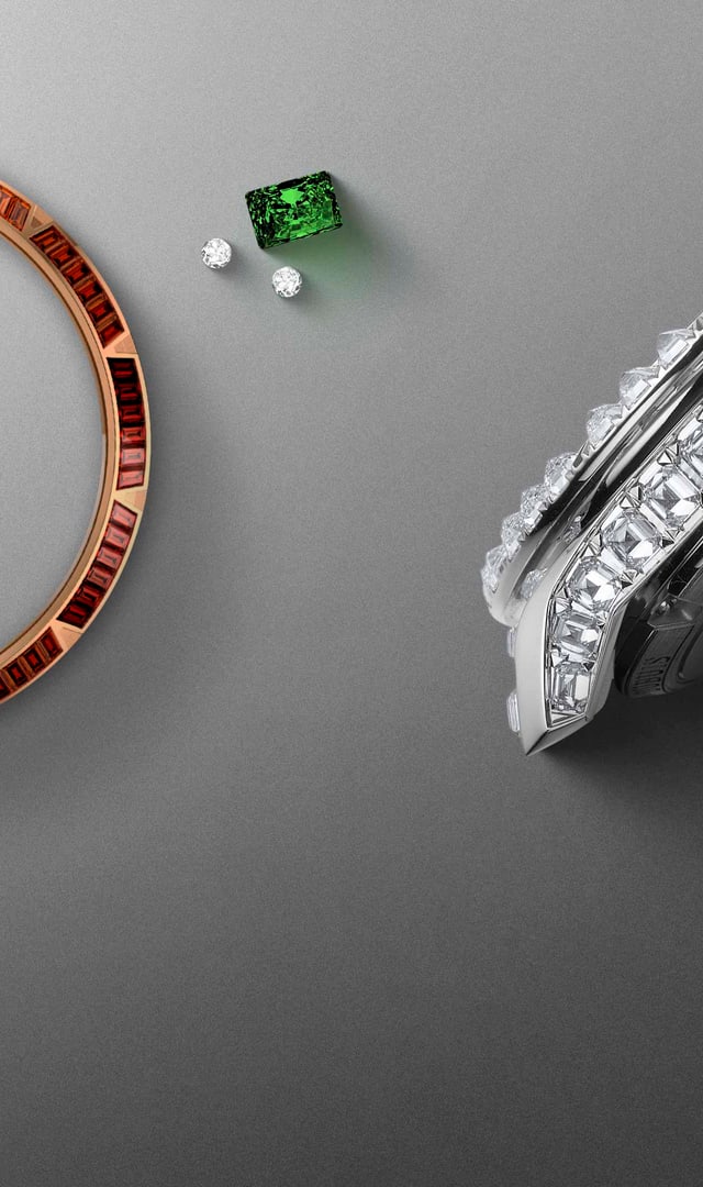 The image features two bezels set with precious stones, a bezel set with stones, individual stones (emeralds, diamonds, sapphires) and part of a diamond-encrusted bracelet, all arranged on a grey surface with tweezers.